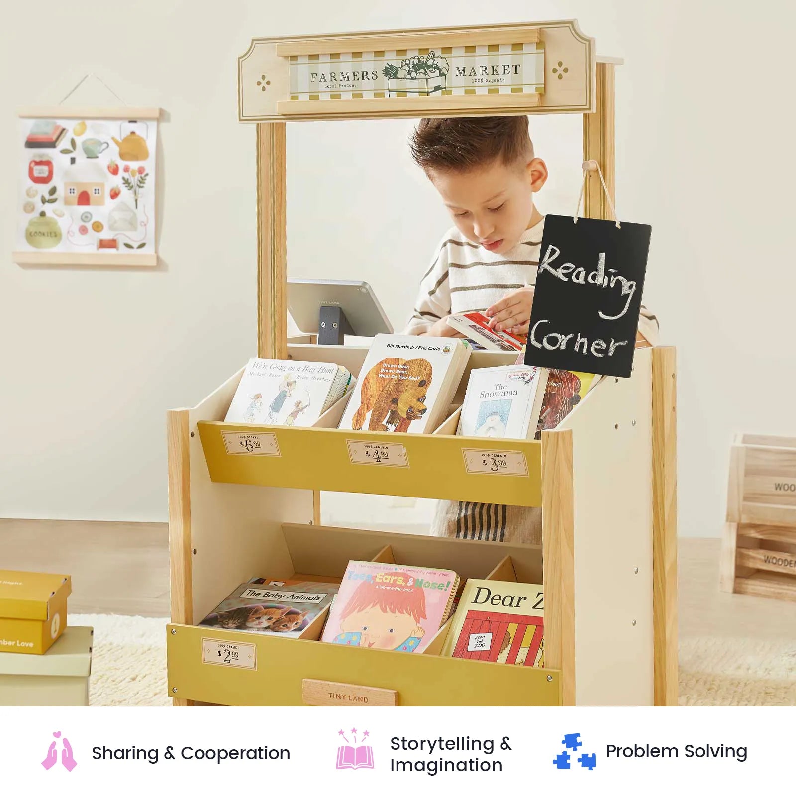 A young child stands at the Tiny Land Farmers’ Market Gift Set: Market Stall & Organic Food Collection, browsing picture books displayed on the wooden stand. The cozy, well-lit classroom is decorated with educational touches and features a role play cash register nearby—perfect for inspiring imaginative shopkeeper games and bringing the kids farmers market toy experience to life.