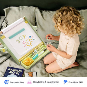 A young child sits on a bed using the Tiny Land® Double-Sided Magnetic Tabletop Easel as their kids’ art station, drawing colorful pictures and letters. The setup features a book, markers, alphabet magnets, and a magnetic whiteboard for endless creative possibilities. Icons below highlight key benefits: concentration, storytelling, and fine motor skills—all from Tiny Land.|Green