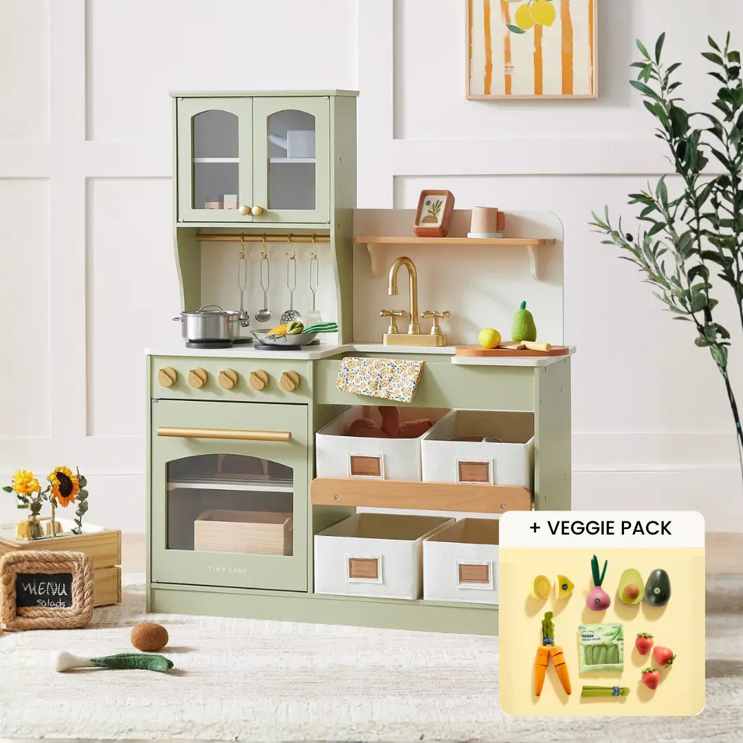 The Tiny Land® Smart Storage Kitchen Harvest Set by Tiny Land features a pastel green wooden play kitchen with utensils, pots, a bowl, baskets, and play food. Shown: toy veggies from the veggie pack. Sunflowers and wall art brighten the background.