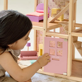 A young child plays with the Tiny Land® Sweetwood Unicorn Dollhouse by Tiny Land, opening a small pink door. This wooden dollhouse includes miniature furniture, poseable dolls, and a charming staircase inside.