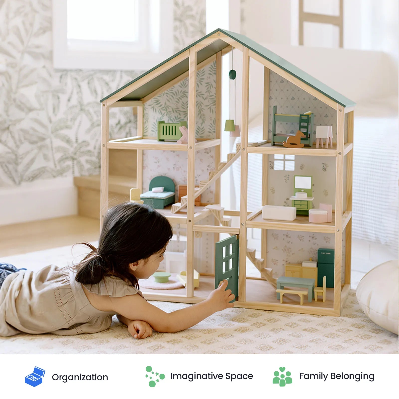 A young child plays on the floor with the Tiny Land® Sweetwood Dollhouse without Dolls, thoughtfully arranging furniture inside. The softly lit room, adorned with patterned wallpaper, radiates calm and inspires creativity. This classic Tiny Land toy encourages imaginative play, as icons below emphasize organization, imagination, and family.|green