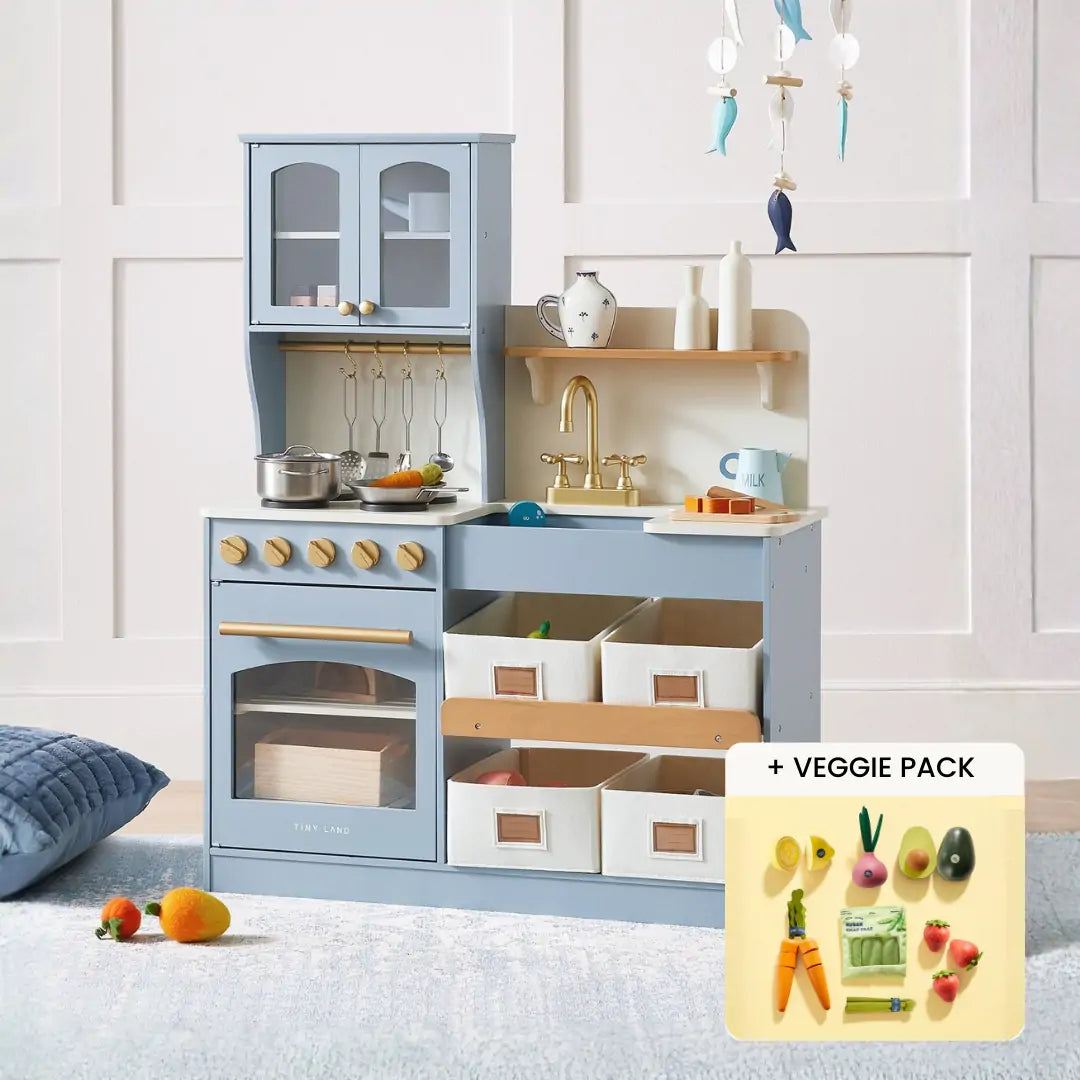 The Tiny Land® Smart Storage Kitchen Harvest Set by Tiny Land is a light blue wooden play kitchen with stovetop, oven, sink, shelves, storage bins, plus pots, utensils, and toy veggies like carrots and avocado—ideal for pretend play.