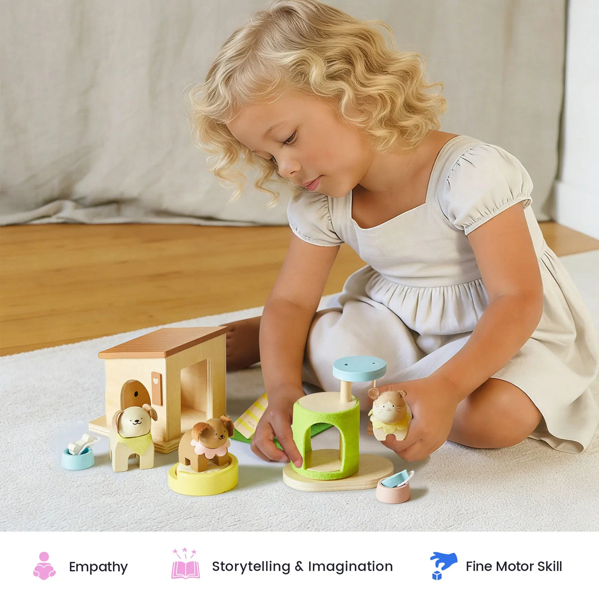 A young child in a white dress plays with the Tiny Land® Happy Urban Paws wooden pet playset and miniature houses on a white rug. Icons below highlight benefits: empathy, storytelling & imagination, and fine motor skill.