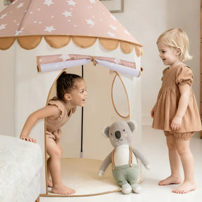 Two young children play near the Tiny Land® Cheerful Pennant Castle Tent by Tiny Land. One smiles inside the kids’ playhouse while the other stands outside. A plush koala toy is placed at the tent’s entrance.