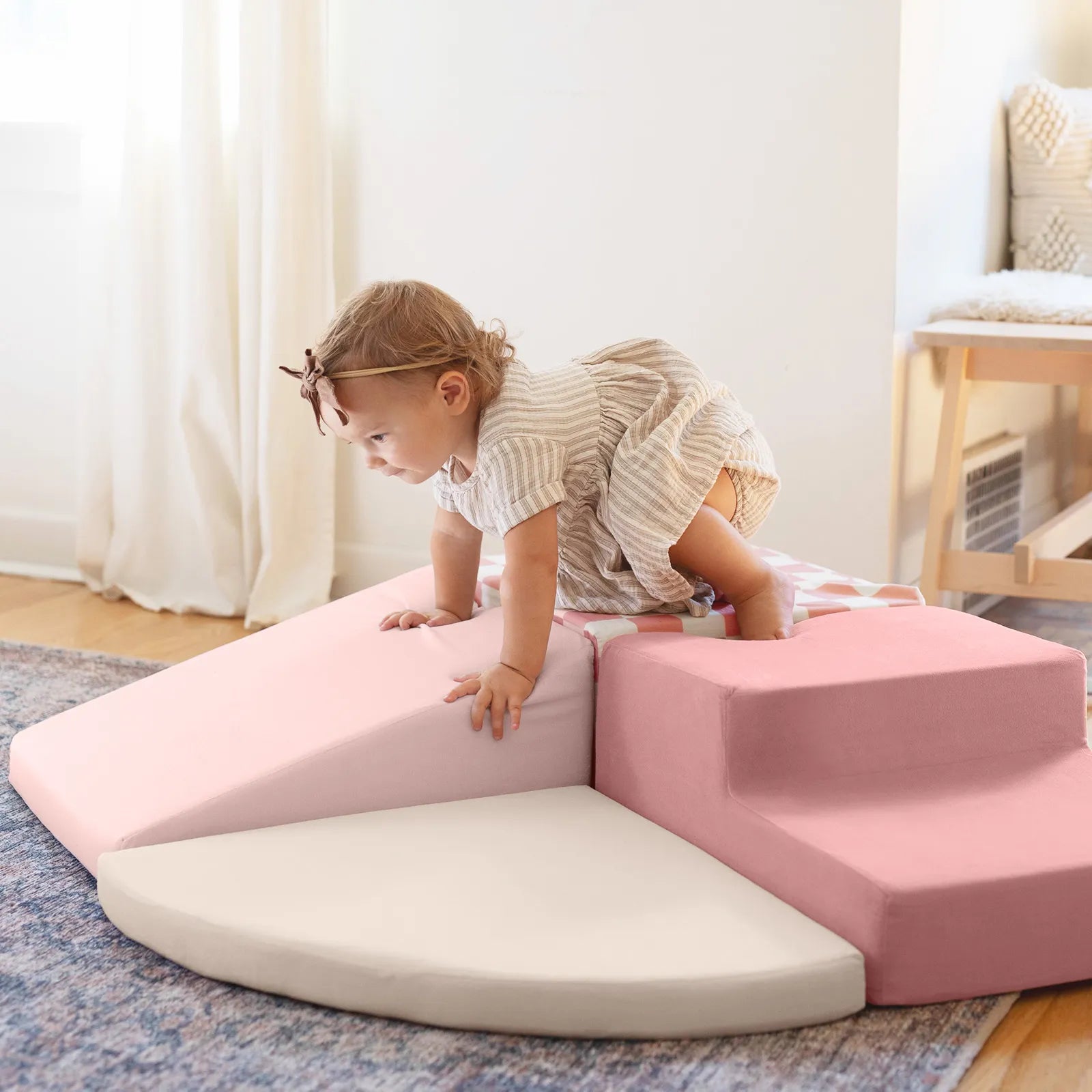 A young child in a striped dress crawls on the Tiny Land® PlayNest Climbing Blocks, enjoying safe fun in a bright, cozy room with natural light and a blue rug.