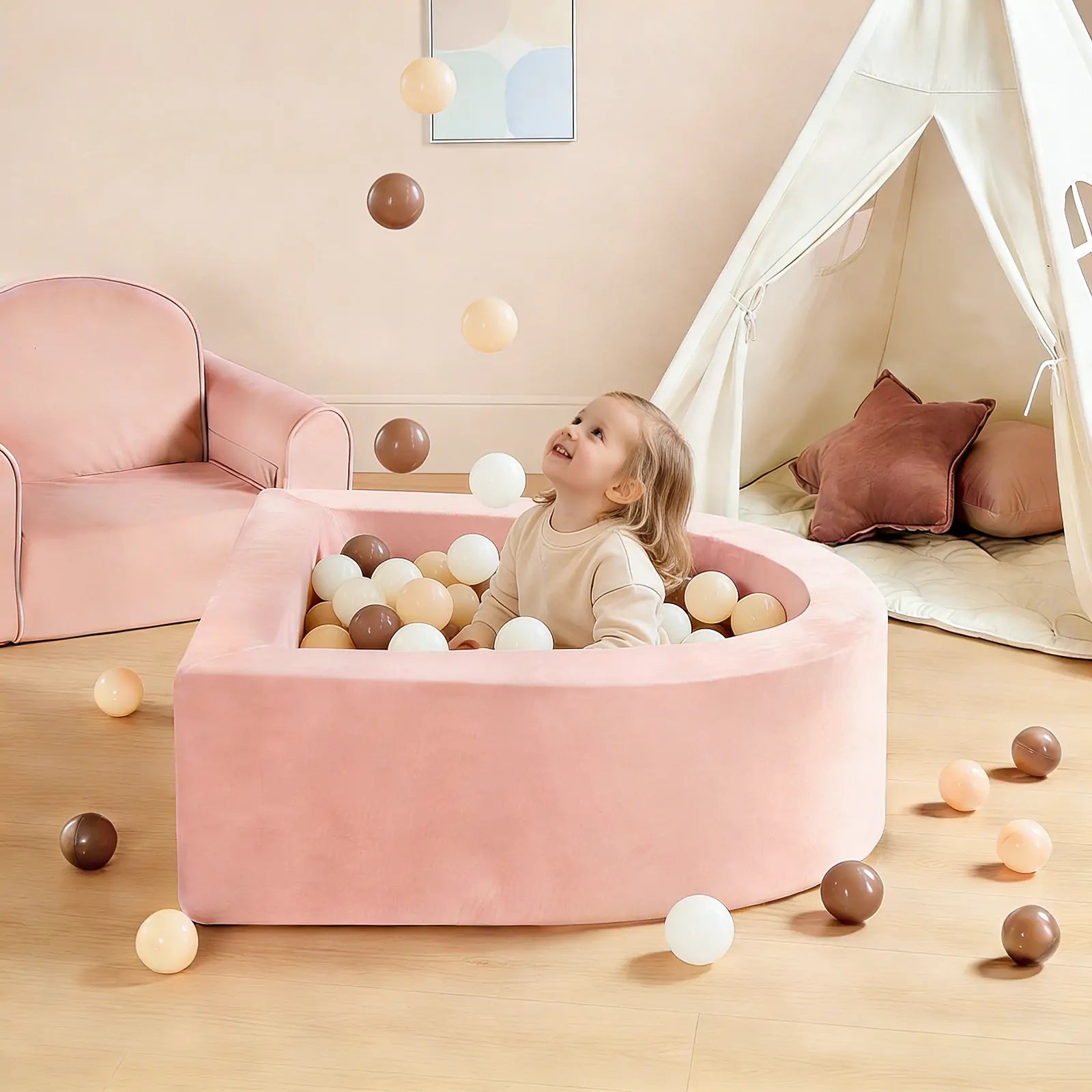 A young child enjoys playtime in the Tiny Land® Pink PlayNest Ball Pit by Tiny Land INC, surrounded by beige, white, and brown balls. In the background are a pink armchair and a white play tent with pillows.|pink