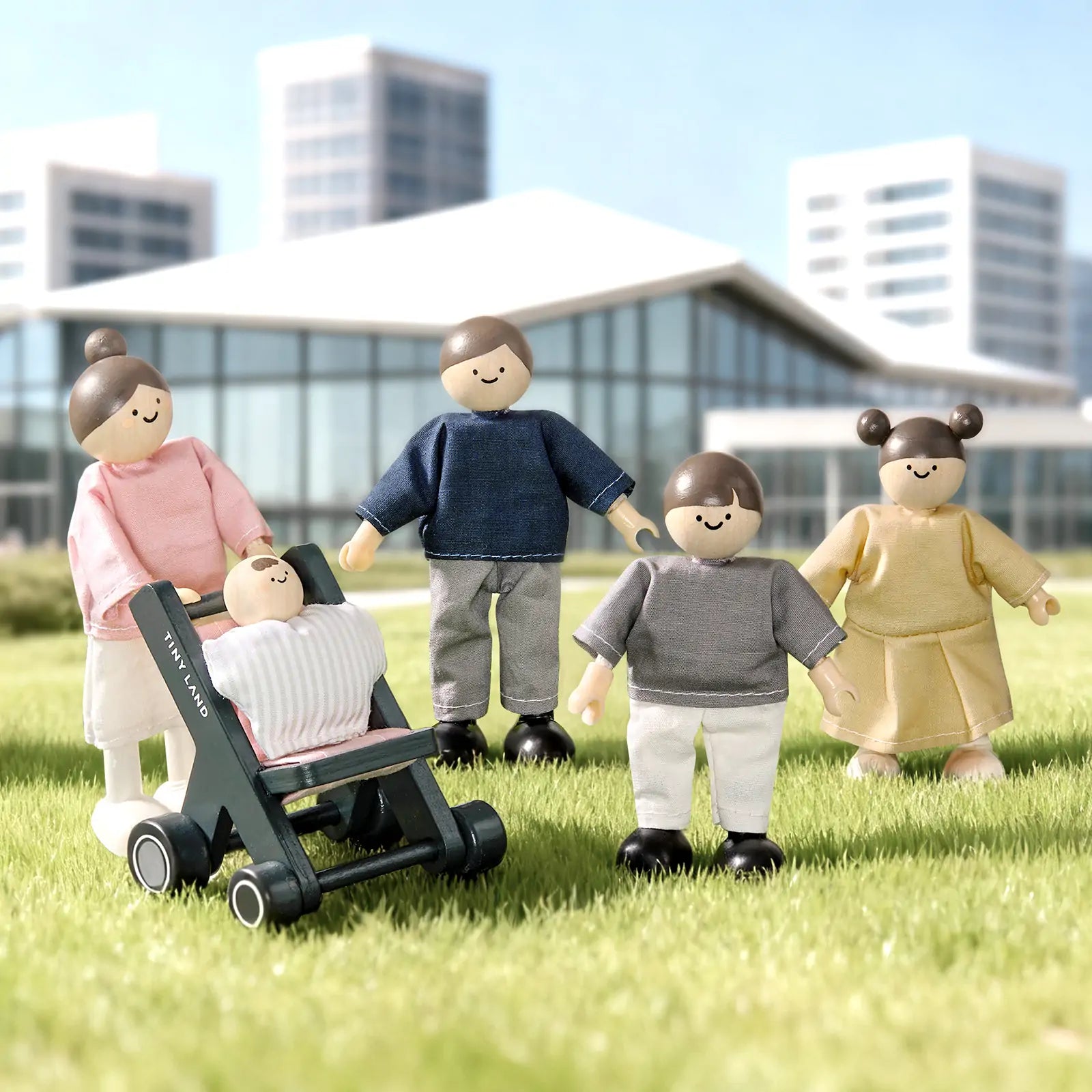 Four Tiny Land® Wooden Dollhouse Dolls, including one in a stroller, stand on grass with modern buildings behind them. These 1:12 scale dolls by Tiny Land are dressed casually and resemble a family enjoying time outdoors.