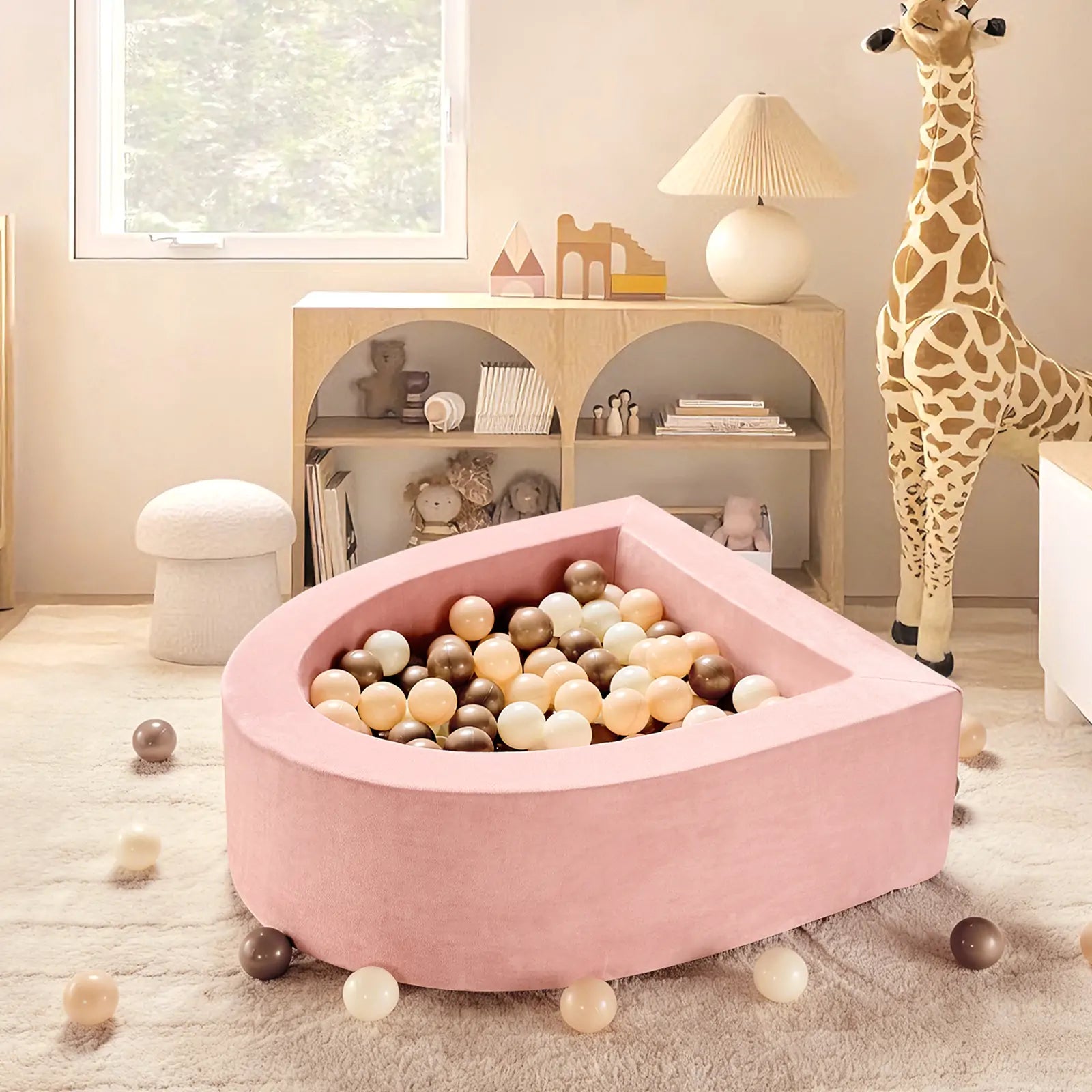 A cozy children's playroom featuring the Tiny Land® Pink PlayNest Ball Pit by Tiny Land INC (Ocean Balls not included), a large giraffe plush toy, pastel decor, a bookshelf, and soft, neutral-toned furniture.|pink