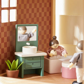 The Tiny Land® Sweetwood Pegasus Dollhouse bathroom scene features a green sink, potted plant, mirror, and wooden poseable family dolls—one in a bathtub holding a baby, another standing nearby—all from Tiny Land.