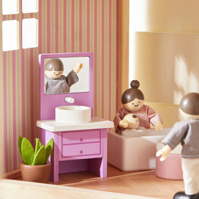 Two poseable Tiny Land® Wooden Dollhouse Dolls enjoy the bathroom in the Sweetwood Unicorn Dollhouse—one relaxes in a white tub holding a baby doll, while the other stands nearby amid a purple sink, round mirror, and green potted plant.