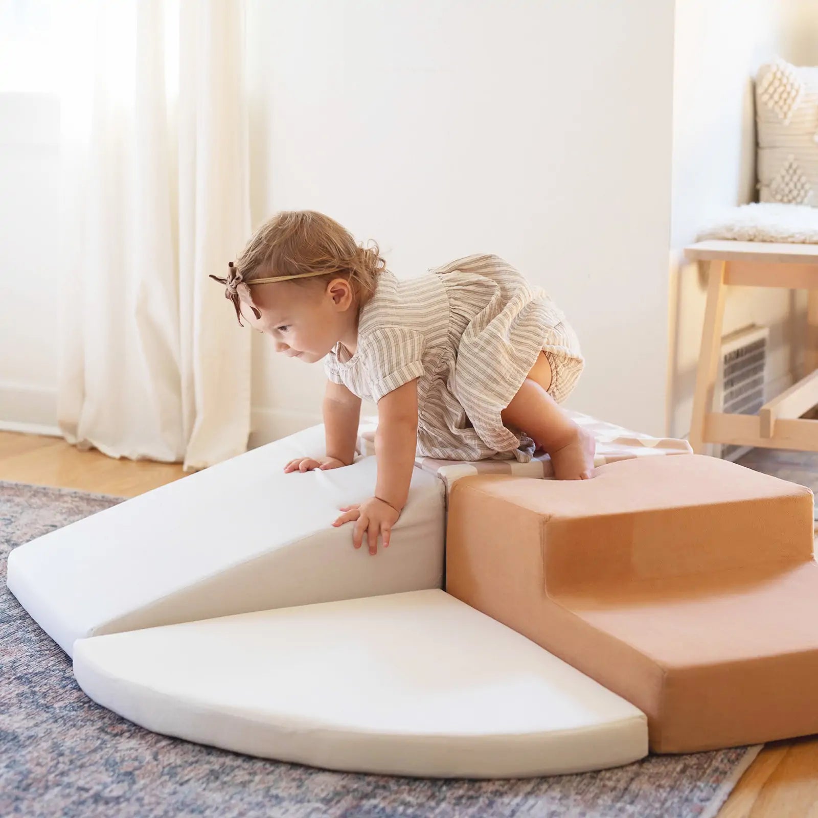 A toddler in a striped dress climbs on the Tiny Land® PlayNest Climbing Blocks by Tiny Land INC, building gross motor skills in a bright, cozy room filled with sunlight.