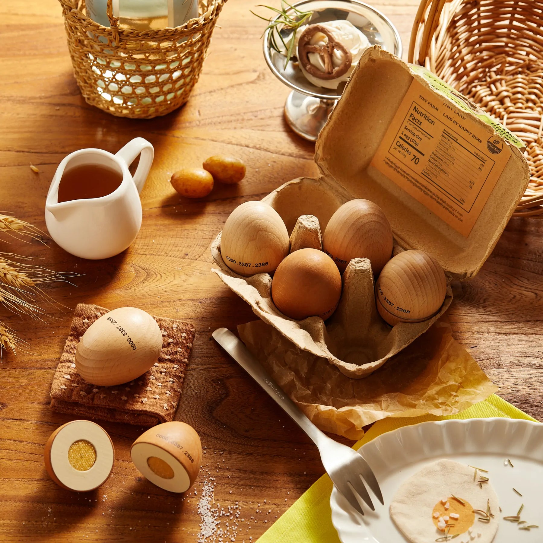 The Tiny Land® Organic Play Food - 4 Sets by Tiny Land features brown wooden eggs in a carton on a wooden table, surrounded by play accessories, creating a charming rustic breakfast scene with pretend food toys.