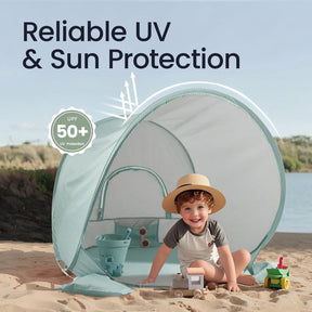 A smiling child in a sunhat enjoys the Tiny Land® One-Stop Beach Toy & Tent Set – Sea Blue, sitting in the tent with sand tools by water and greenery. Image text: Reliable UV & Sun Protection, UPF 50+ UV Protection. Brand: Tiny Land.