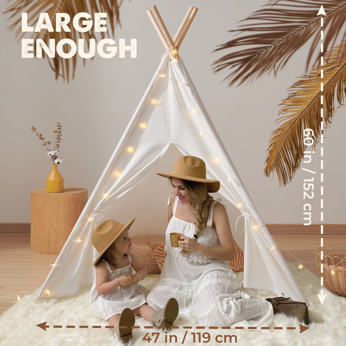 A woman and child in hats sit inside the Tiny Land Vibrant Imaginative Retreat Set—featuring a colorful easel and kids teepee (60 in/152 cm tall, 47 in/119 cm wide)—decorated with string lights on a fluffy rug beside palm leaves.