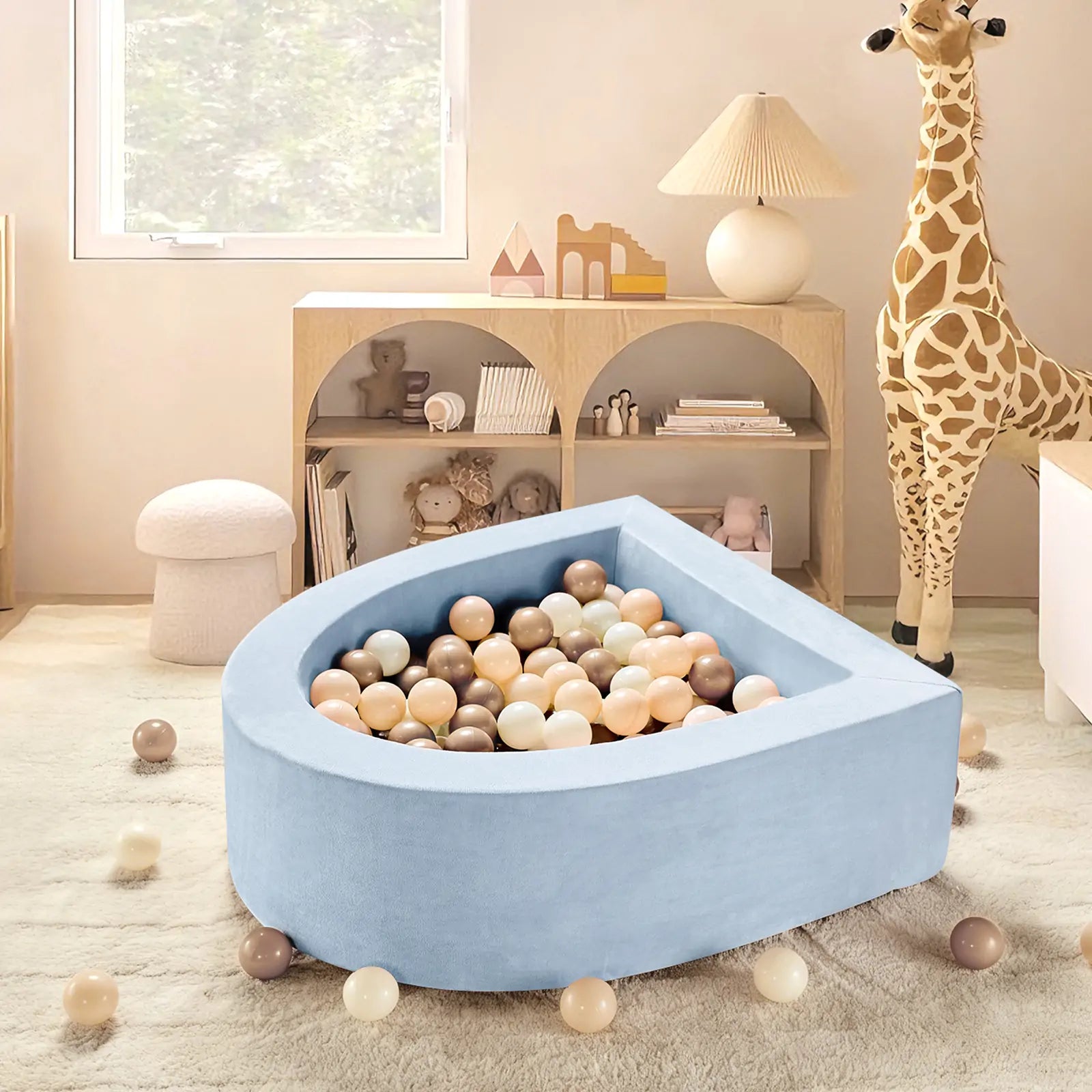 The Tiny Land® Blue PlayNest Ball Pit with 200 Ocean Balls by Tiny Land INC sits in a neutral playroom with a plush giraffe, round stool, window, and shelves of toys and books. The light blue, teardrop-shaped pit is filled with pastel ocean balls.|blue