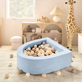The Tiny Land® Blue PlayNest Ball Pit with 200 Ocean Balls by Tiny Land INC sits in a neutral playroom with a plush giraffe, round stool, window, and shelves of toys and books. The light blue, teardrop-shaped pit is filled with pastel ocean balls.|blue