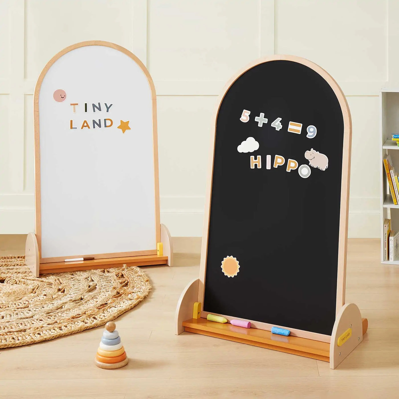 Two Tiny Land® Double-Sided Arched Magnet Chalkboards stand side by side—one showcasing colorful "Tiny Land" letters, the other decorated with math magnets, "Hippo," and doodles. Chalk and erasers are nearby for creative fun.