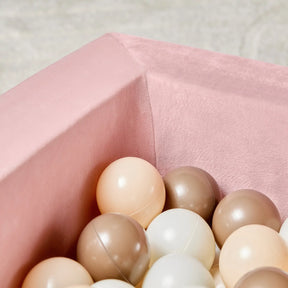 A close-up of the Tiny Land® PlayNest Ball Pit by Tiny Land, velvet-lined in pink and filled with 200 pastel ocean balls in cream, beige, and brown—perfect for creating a cozy toddler play space against a soft, neutral backdrop.|Pink