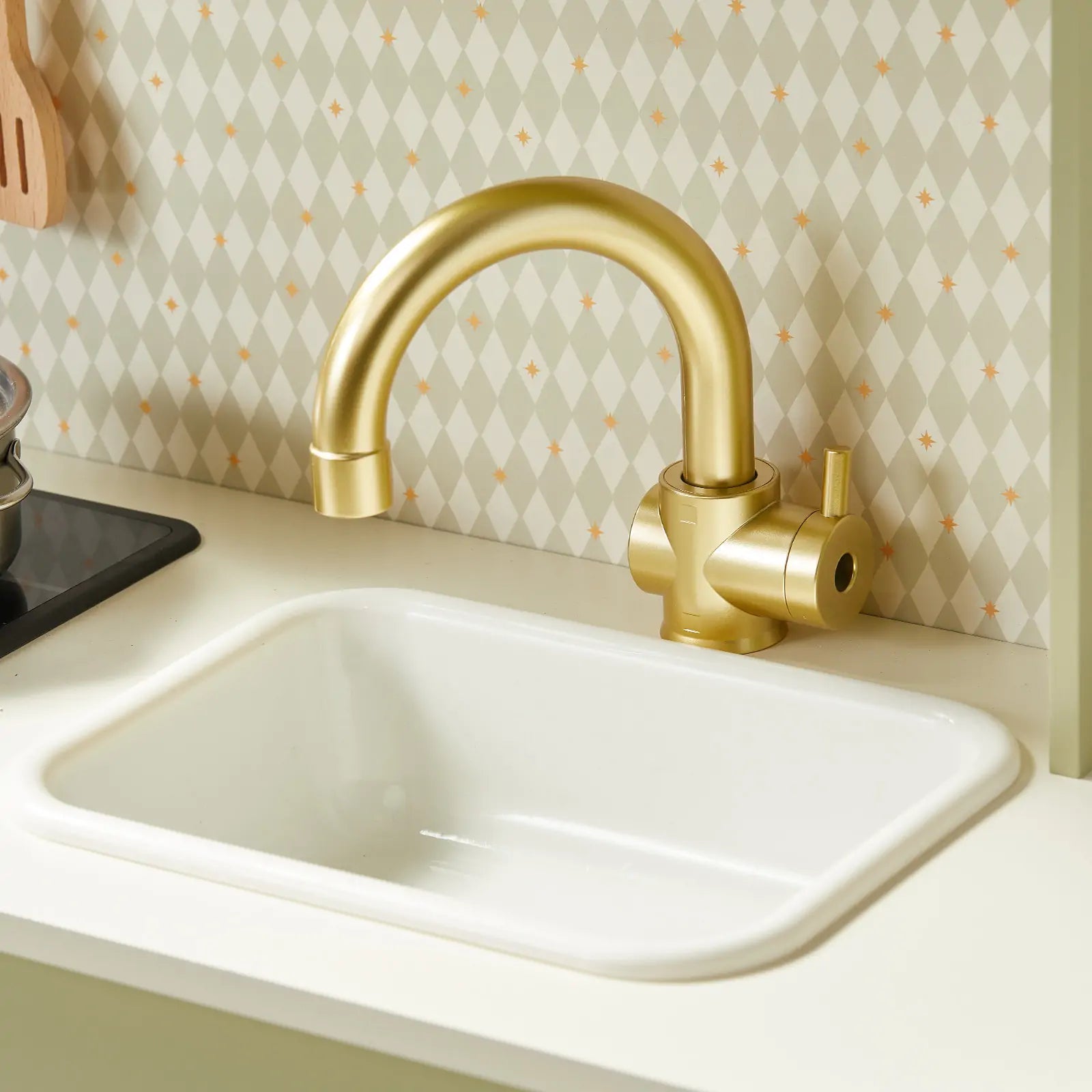The Tiny Land® PopJoy Play Kitchen - Green features a white sink with a gold faucet set in a light countertop, perfect for kids. A geometric diamond-patterned backsplash in soft tones adds style to this Tiny Land playset.