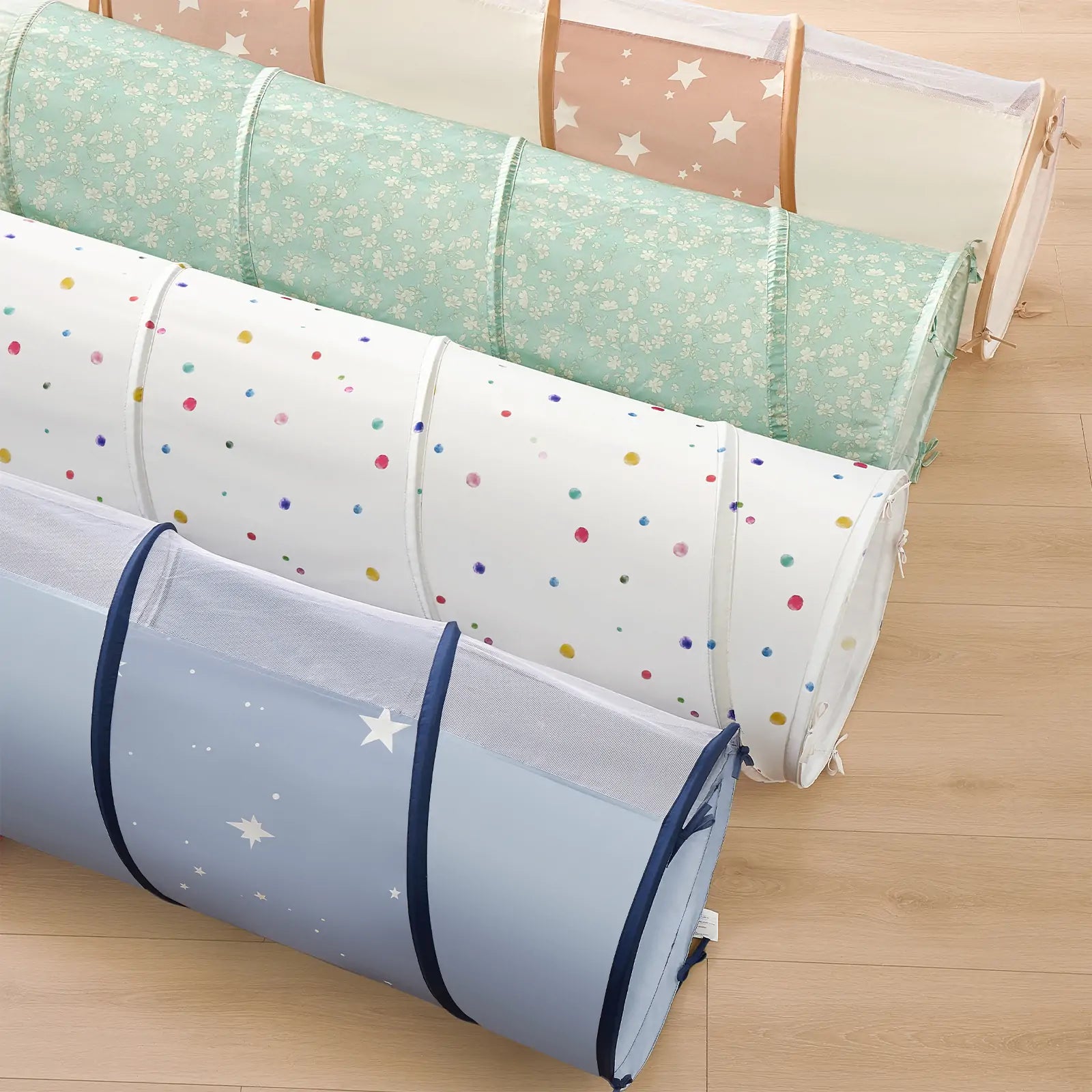 The Tiny Land® Adventure Play Tunnel by Tiny Land, featuring colorful polka dots and mesh panels, is showcased rolled up with other pastel kids’ tunnels on a light wooden floor.