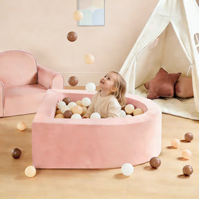 A young child enjoys the Tiny Land® PlayNest Climbing Ball Pit Set with Tunnel, filled with pastel balls. Nearby is a soft pink armchair, play tent, and climbing blocks from Tiny Land, creating a cozy indoor playground.