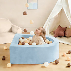 A young child smiles in the Early Bird Eggs-Tiny Land® PlayNest Ball Pit with 200 Ocean Balls by Tiny Land INC, tossing pastel balls in the air. A beige sofa, white teepee, and soft decor create a cozy play space behind them.|blue