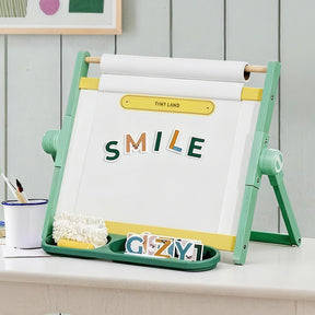 The Tiny Land® Double-Sided Magnetic Tabletop Easel - Green by Tiny Land displays "SMILE" with colorful magnetic letters on a whiteboard. A tray below holds extra letters, a white eraser, and a cup of paintbrushes for creative fun.