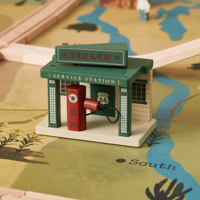 A small wooden Texaco service station with a red gas pump sits on the Tiny Land® 1920 Railway Adventure Train Table by Tiny Land INC, featuring map-themed play, a blue “South” river, and vintage-style wooden train tracks in the background.