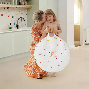A smiling woman in a polka dot dress hugs a giggling girl holding the Tiny Land® Adventure Play Tunnel—Colorful Polka Dots, a fun play tunnel from Tiny Land that pairs perfectly with matching mats for extra indoor excitement.|white