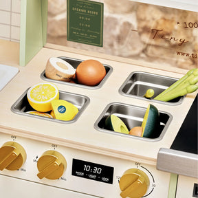 The Tiny Land® BistroSwitch Play Kitchen by Tiny Land features four metal trays with wooden lemon, onion, cucumber, and asparagus. Ideal for pretend play, it has gold knobs and a digital timer display set to 10:30.|Green