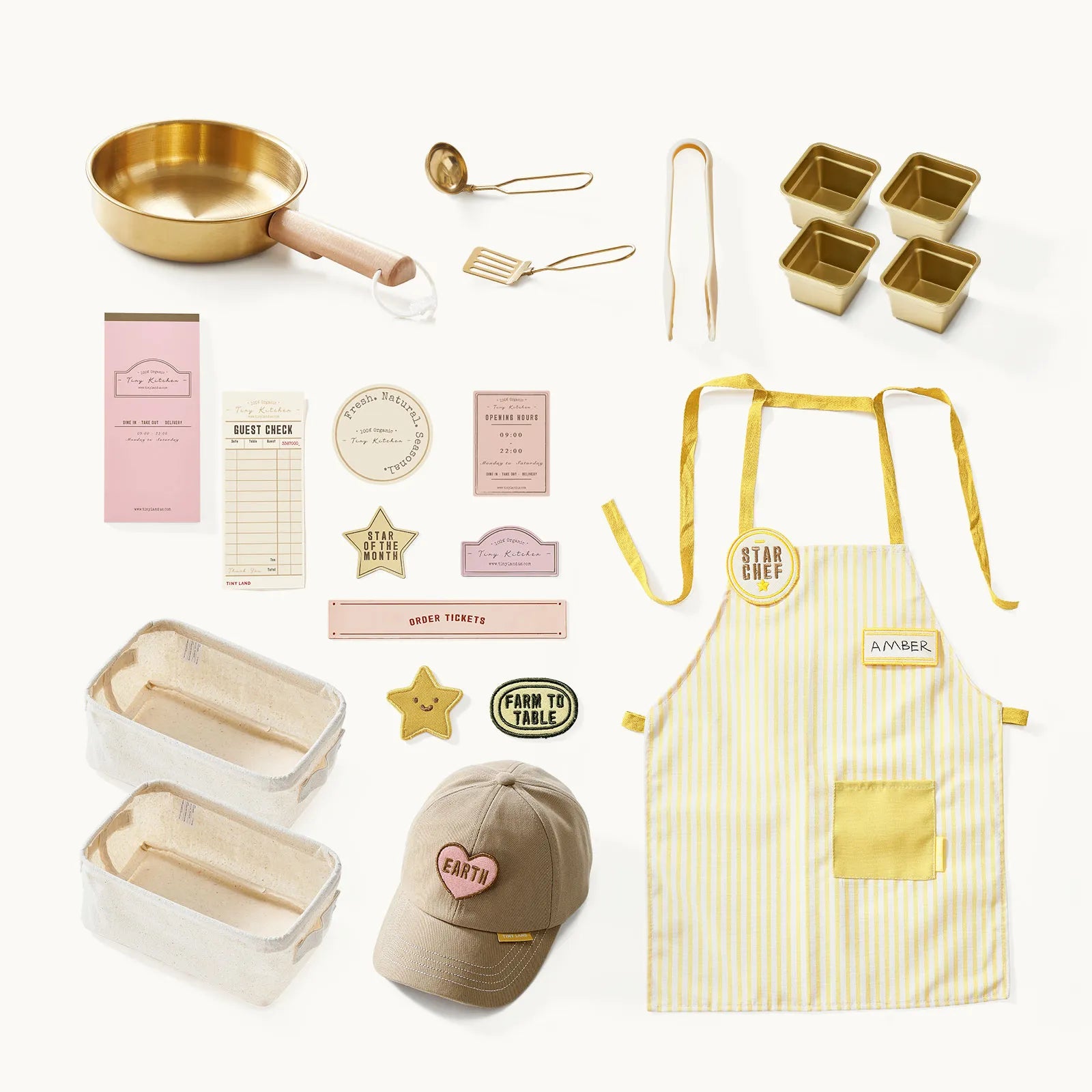 A flat lay of Tiny Land® BistroSwitch Play Kitchen accessories by Tiny Land, including gold tools, mini loaf pans, a yellow-striped apron, beige cap, cloth baskets, recipe cards, paper tags, and star pins on a white background.|White