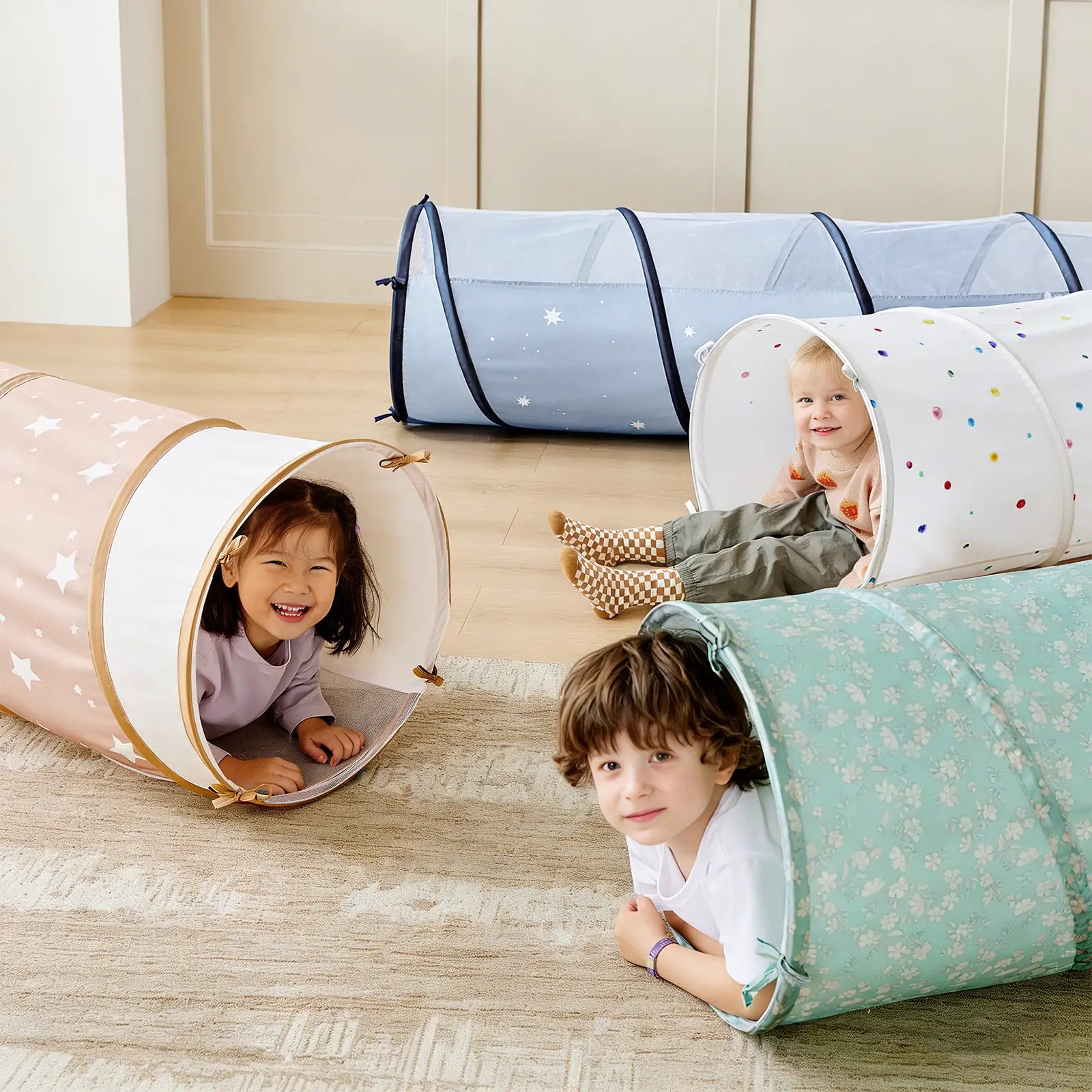 Three young children smile as they play inside the Tiny Land® Adventure Play Tunnel - Green by Tiny Land. Decorated with stars, dots, and floral patterns, this colorful tunnel creates a bright and cheerful scene on a light wood floor.