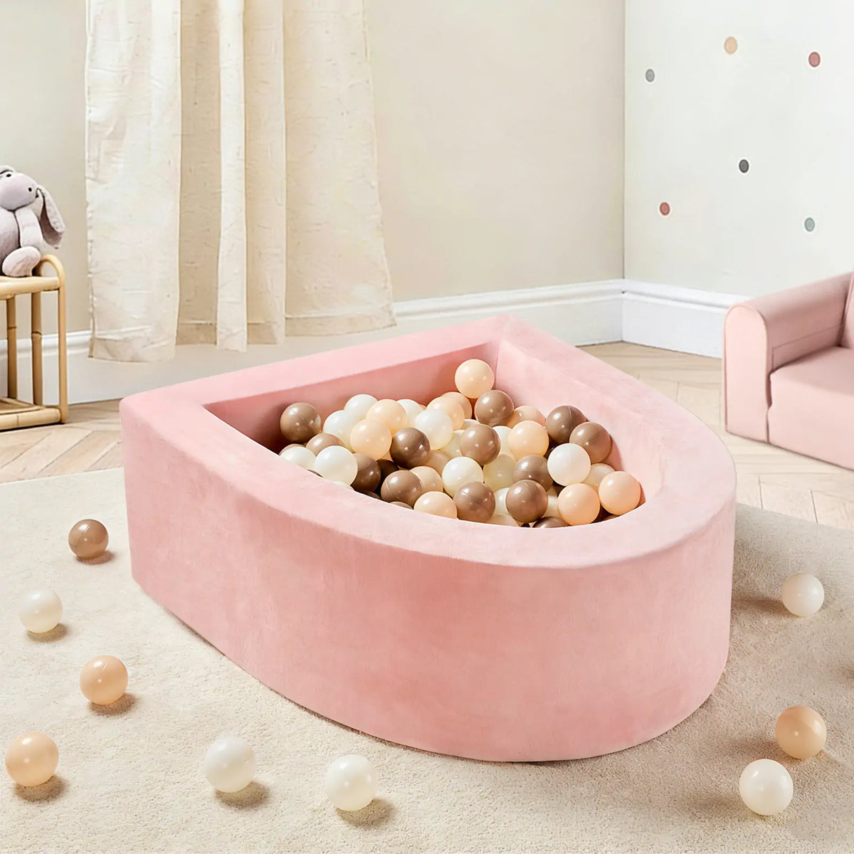 The Tiny Land® Pink PlayNest Ball Pit with 200 Ocean Balls by Tiny Land sits in a cozy, light-toned children’s room, with pastel balls scattered on the wooden floor near a small pink sofa and a plush bunny toy on the shelf by the window.