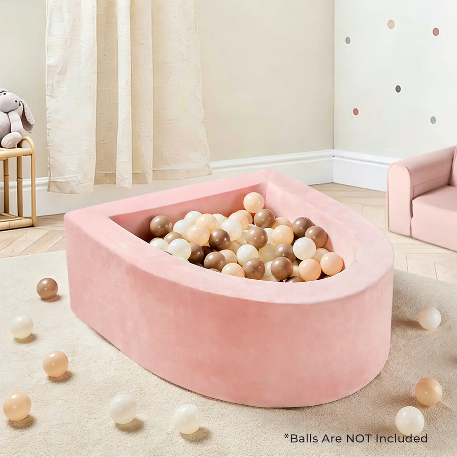 The Tiny Land® PlayNest Soft Foam Ball Pit—shown here in pink and styled with beige, cream, and brown balls (balls not included)—makes a perfect sensory play spot for any pastel-themed child's room. Loose balls are scattered on the floor. Text reads: *Balls Are NOT Included. Add coordinating Tiny Land climbing blocks for even more fun!.|Pink