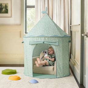 A young child sits inside the Tiny Land® Tiny Sprout Castle Tent, a pastel blue playhouse with floral patterns, holding a stuffed elephant. The tent by Tiny Land is set up on soft mats in a cozy, well-lit room.