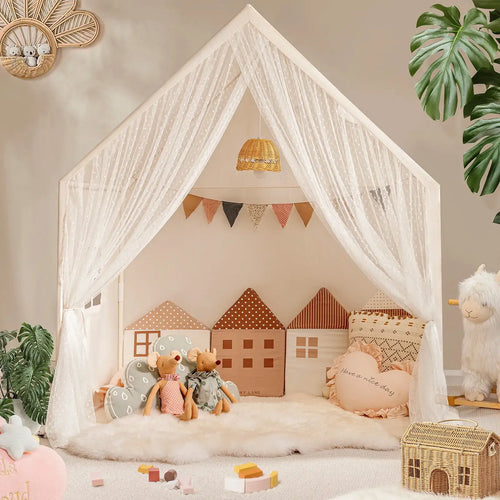 The Tiny Land® Chef’s Corner Playset features a cozy cream playhouse and kitchen set, complete with sheer white curtains, house-shaped pillows, stuffed animals, soft rugs, toys, and plants in a warmly decorated room.