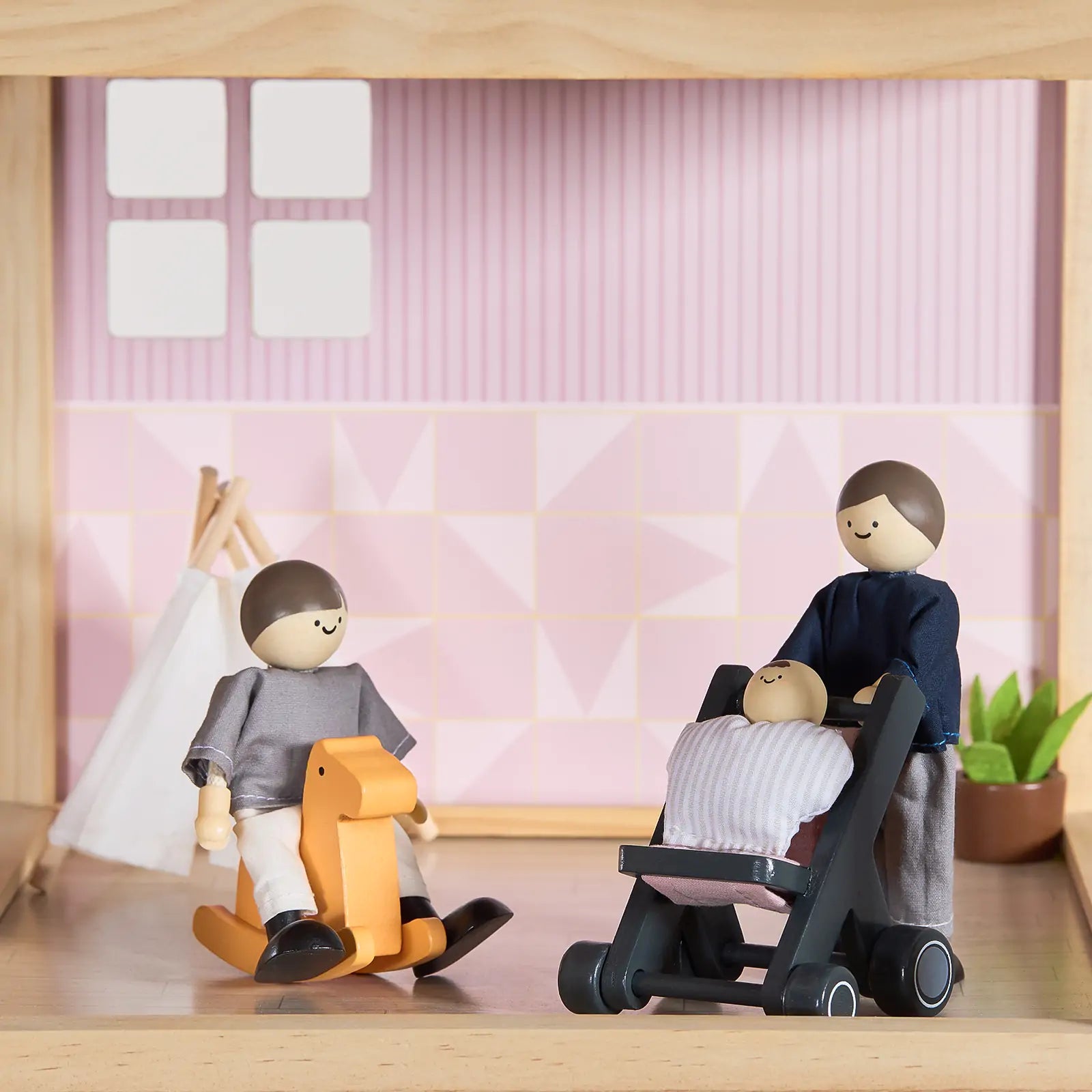 Three Tiny Land® Sweetwood Love Dollhouse & Wooden Dollhouse Dolls from Tiny Land INC enjoy imaginative play in a cozy room with pink patterned walls, a teepee, and a small plant—one rocks on a horse while another pushes the baby in a stroller.