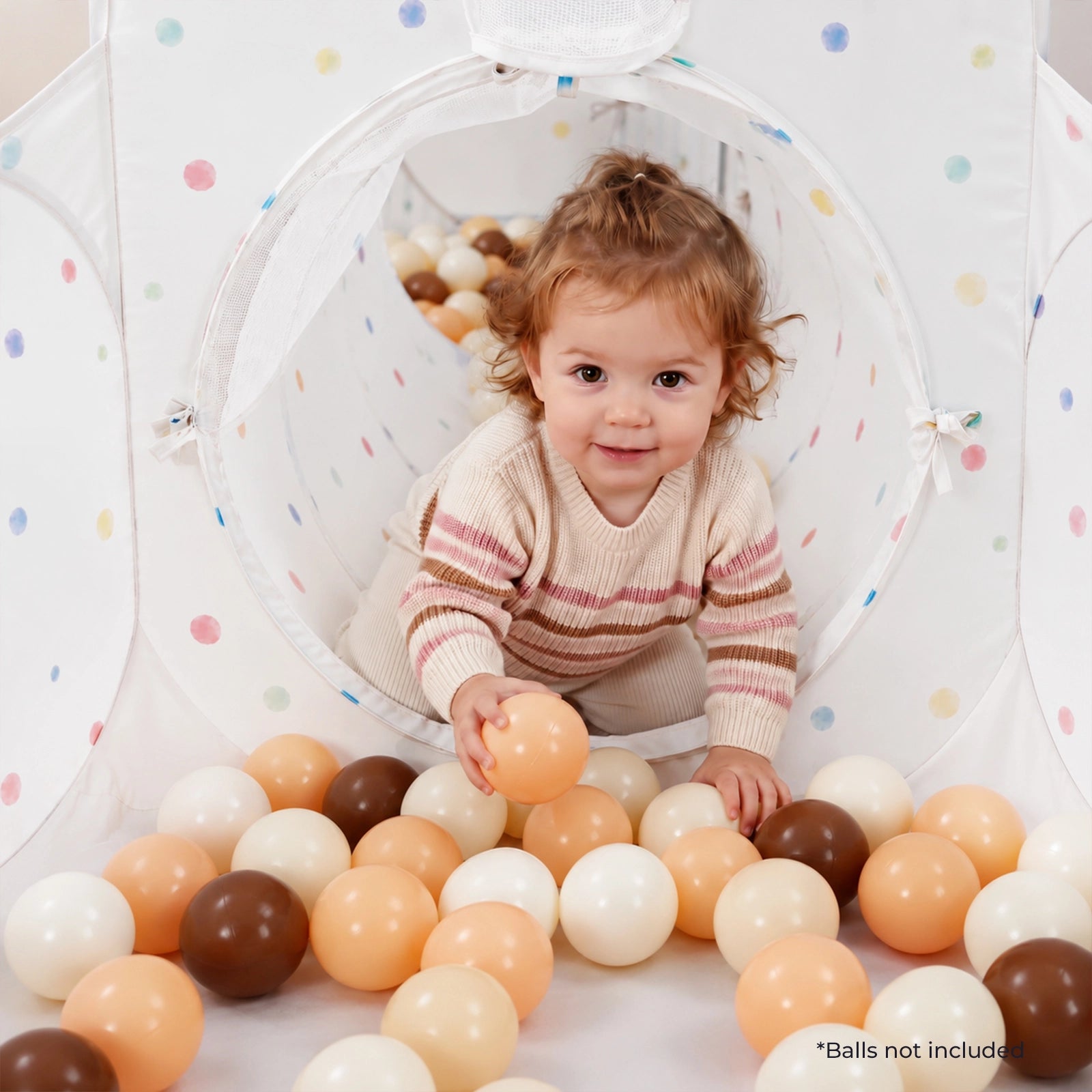 A toddler crawls out of a white, polka-dot Tiny Land® Compact Adventure 3-in-1 Play Tunnel and reaches for a plastic ball on the floor of the play tent.|Colorful Dots