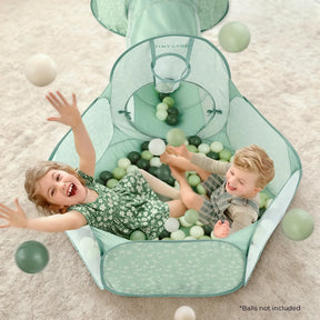 Two young children play joyfully in a floral pastel green Tiny Land® ball pit with a tunnel, tossing Tiny Land® Green Ocean Balls (200 pcs, balls sold separately) into the air. Text reads: *Balls not included.