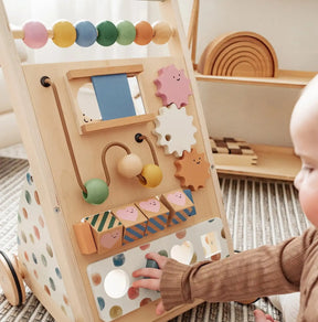 A baby enjoys exploring the Tiny Land Complete Development Playset — Baby Walker + Activity Cube on a carpeted floor, interacting with its colorful beads, gears, blocks, and mirror to build fine motor skills in a fun and Montessori-inspired way.