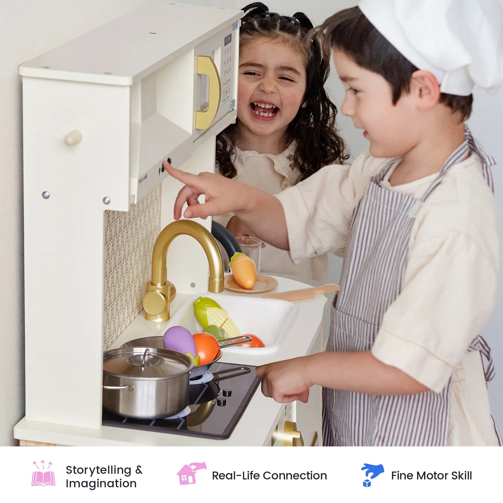 Two children play happily at the Tiny Land® PopJoy Play Kitchen. One boy in a striped apron cooks with pretend play food while a girl smiles behind him. Icons at the bottom highlight benefits like imagination, real-life connection, and motor skill development from Tiny Land.