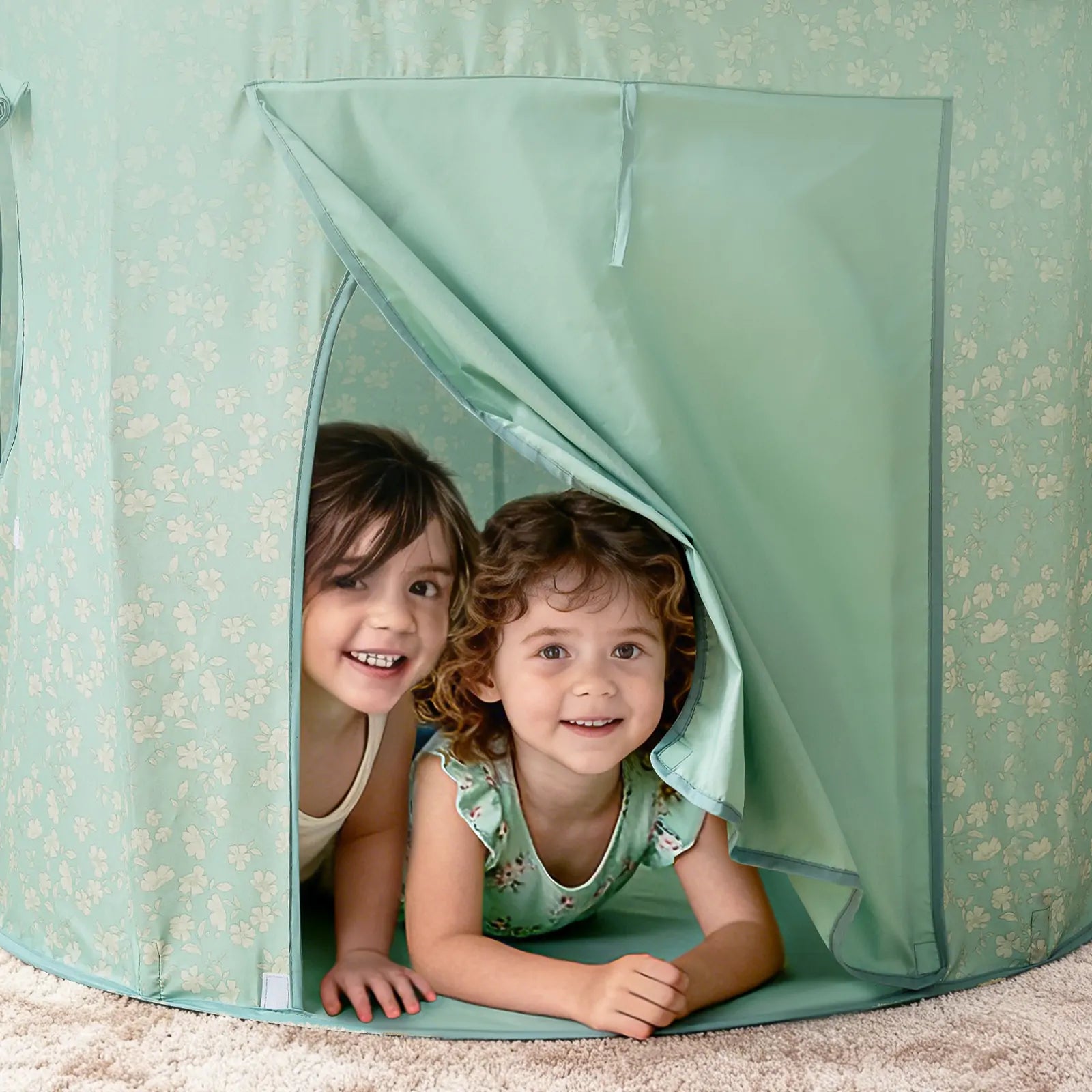 Two young children smile as they lie on their stomachs inside the Tiny Land® Tiny Sprout Castle Tent, peeking out through the open flap onto a beige carpet.