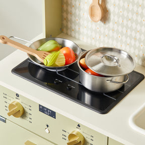 Two metal pots from the Tiny Land® PopJoy Play Kitchen (Pink / Green) sit on the stovetop; one with a lid, both filled with toy vegetables. A wooden spoon rests in the open pan. This charming setup by Tiny Land is perfect for inspiring pretend play adventures.|Sage