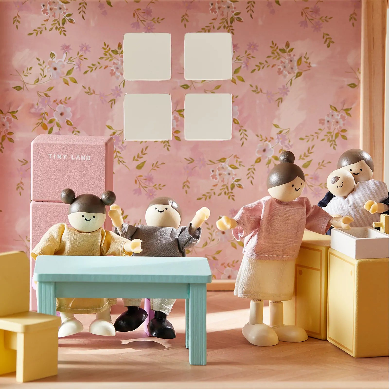 Four poseable Tiny Land® Sweetwood Unicorn Dollhouse dolls with painted faces are set in a pastel-colored kitchen and dining area, featuring a blue table, yellow chairs, and floral wallpaper.