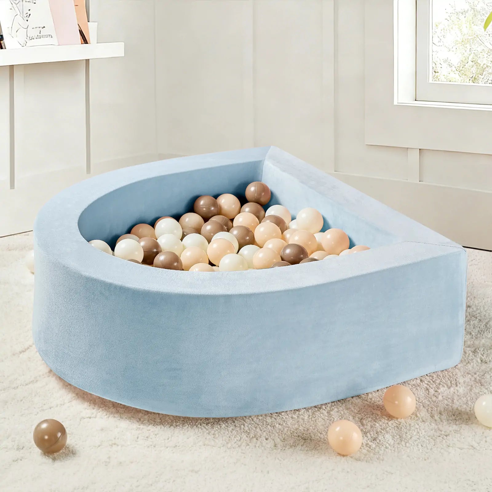 A Tiny Land® PlayNest Ball Pit with 200 beige, brown, and white ocean balls sits on a white carpet in a bright, modern room. A few balls are scattered nearby, creating a playful toddler area.|Blue