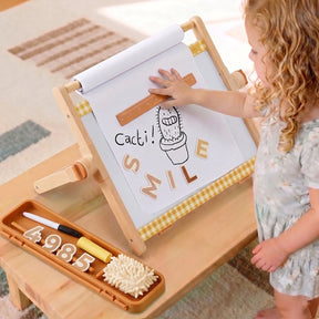 A young child touches a drawing of a cactus labeled "Cacti!" and "SMILE" on the Tiny Land® Double-Sided Magnetic Tabletop Easel by Tiny Land, with markers and numbers placed in the tray on the wooden table.|Oatmeal
