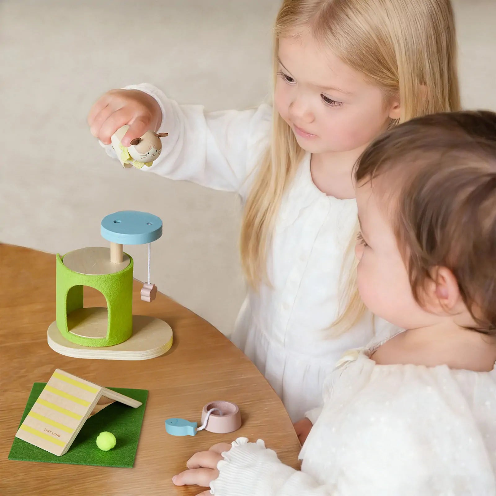 Two young children play at a wooden table with the Test Early Bird Eggs-Tiny Land® Happy Urban Paws set, featuring a green and blue mini pet house, cute accessories, a card, and animal figures for pretend pet play.