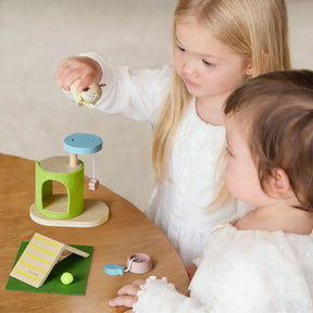 Two young children play at a wooden table with the Test Early Bird Eggs-Tiny Land® Happy Urban Paws set, featuring a green and blue mini pet house, cute accessories, a card, and animal figures for pretend pet play.