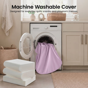 A pink fabric cover from the Tiny Land® GentleSnug Kids Sofa Chair is being placed into a front-loading washing machine in a modern laundry room. Three white foam cushions and a woven basket sit nearby. Text reads: Machine Washable Cover.|Light Purple