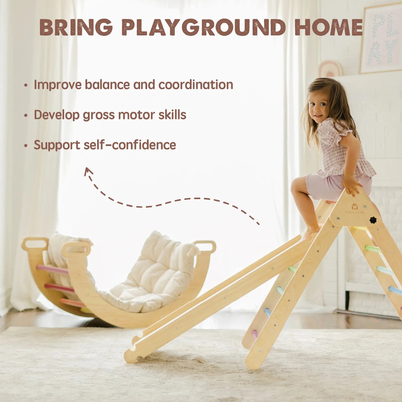 A young girl smiles atop a wooden indoor slide next to the Tiny Land® Pikler Triangle 7-in-1 Montessori Climbing Set. Soft cushions provide comfort as she improves balance, develops motor skills, and builds self-confidence. Brand: Tiny Land.